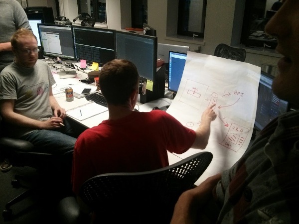 A developer in a red t-shirt points at a diagram while others watch