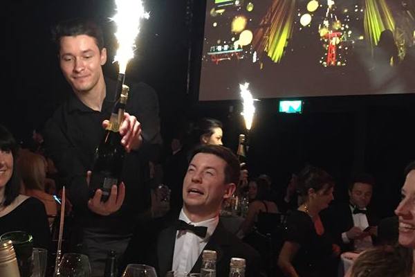 A black tie dressed man wincing at a sparkler